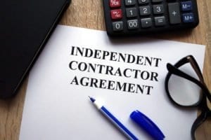 Independent contractor agreement, business, individual, company, employment lawyer, tax act, insurance, pension plan, human rights, GST, health benefits, worker compensation, liability, penalty, contract, calculator, glasses, pen, folder